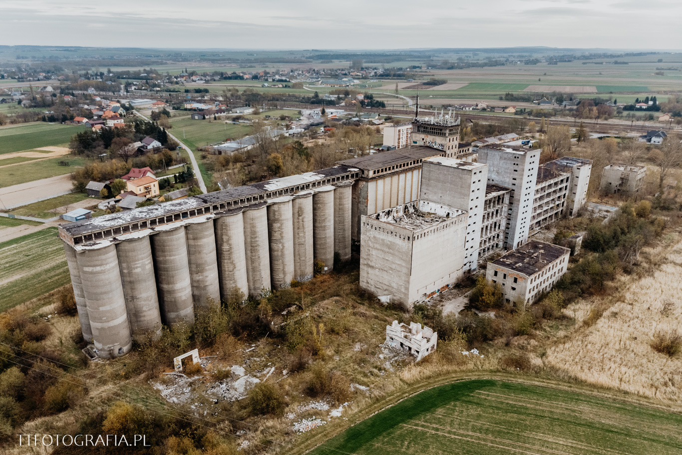 Zespół zakładów zbożowych PZZ w Kozłowie z lotu ptaka: rząd silosów, wieże i hale wśród pól